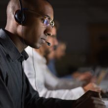 Focused call center operator typing on laptop. African American young man in eyeglasses looking at laptop at workplace. Call center concept