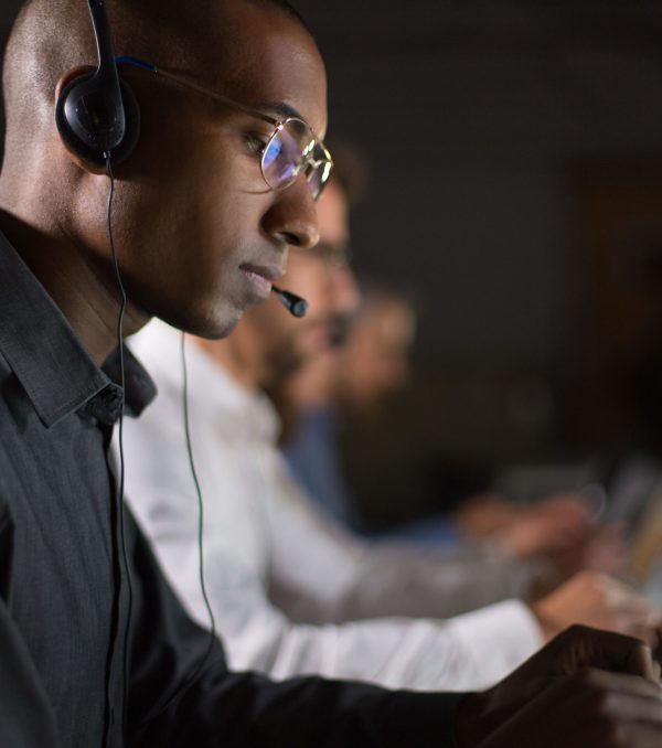 Focused call center operator typing on laptop. African American young man in eyeglasses looking at laptop at workplace. Call center concept